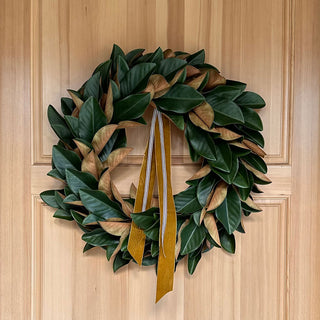 Exquisite 30" Faux Green Magnolia Leaf Wreath by CG Hunter adorning a wooden door with a sophisticated ribbon accent, enhancing the elegance of the entrance.