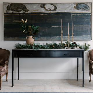 Luxe 6' Magnolia, Eucalyptus, Pinecone, & Needle Pine Garland by CG Hunter elegantly draped on a black console table, complemented by a minimalist decor with an art piece in the background.