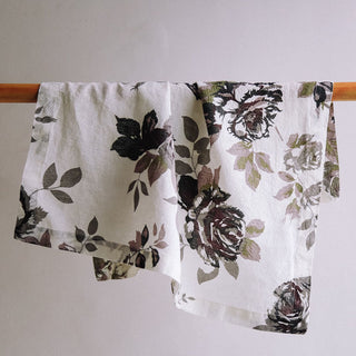 Elegant CG Hunter Eggplant and Grey Roses Napkins displayed on a wooden rod, showcasing intricate grey rose designs on a rich eggplant background for a luxurious dining experience.