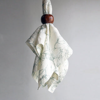 CG Hunter Grey and Green Lilies Napkin elegantly tied with a wooden ring, illustrating its luxurious linen texture and enchanting floral motifs.
