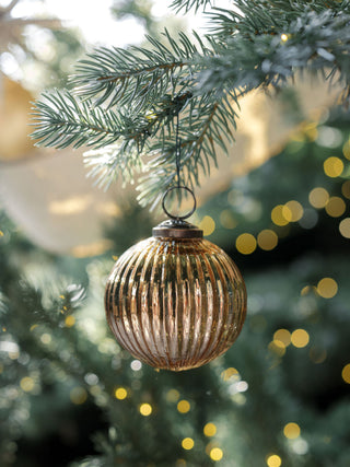 Elegant 4" Mercury Ribbed Glass Antique Gold Ornament by CG Hunter hanging on a Christmas tree, reflecting warm holiday lights for a luxurious festive look.