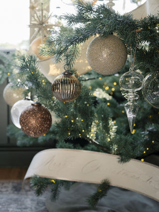 Close-up of decorative elements on a Christmas tree featuring 4" Mercury Ribbed Glass Antique Gold Ornaments by CG Hunter, showcasing exquisite craftsmanship and elegant holiday decor.