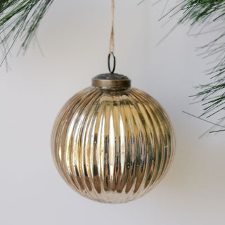 Handmade 4" Mercury Ribbed Glass Antique Gold Ornament by CG Hunter, elegantly hanging amidst evergreen branches, showcasing its exquisite ribbed texture and luxurious antique finish.