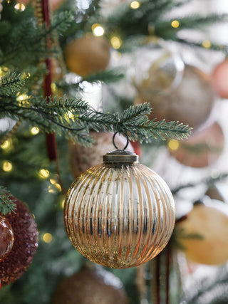 4" Mercury Ribbed Glass Antique Gold Ornament by CG Hunter, beautifully displayed on a festive tree, surrounded by warm holiday lights and other elegant decorations, adding a touch of sophistication.