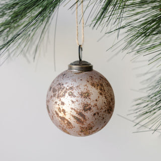 Elegant 3-inch Mercury Marble Glass Ornament by CG Hunter, gracefully hanging from a pine branch, showcasing a stunning taupe gold antiqued finish.