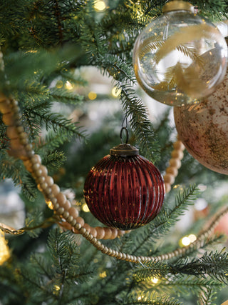 Timeless bordeaux glass ornament by CG Hunter, elegantly hanging on a festive Christmas tree, surrounded by warm lights and decorative garland, epitomizing luxury holiday charm.