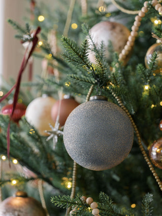 Close-up of a Christmas tree featuring the elegant 5" Textured Slate Blue Glass Ornament by CG Hunter, surrounded by other festive decorations.