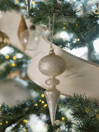 Sophisticated clear glass finial ornament from CG Hunter, showcasing intricate textures in a neutral palette, beautifully hanging among festive decorations.
