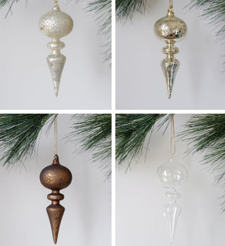 Luxury assorted neutral palette glass finial ornament set by CG Hunter featuring matte, shiny, and clear finishes, elegantly displayed on a pine tree.