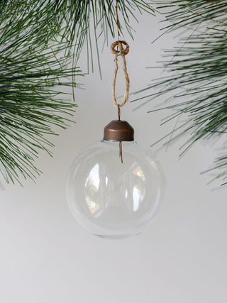 Beautifully crafted 2.25" Clear Glass Ornament by CG Hunter, suspended amidst vibrant pine foliage, showcasing its crystal-clear elegance for festive charm.