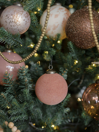 An elegant display of a 3" Flocked Vintage Rose Glass Ornament by CG Hunter among other festive ornaments on a beautifully decorated Christmas tree, adding depth and warmth.