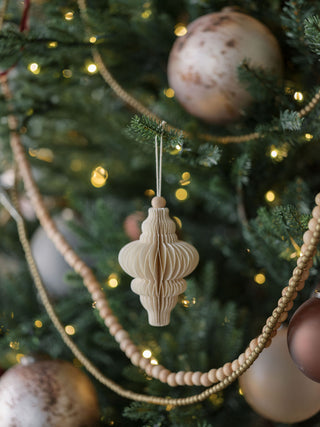 Charming hand-cut paper ornament from CG Hunter, featuring an ornate shape, tastefully hanging amidst a backdrop of luxurious holiday decor on a Christmas tree.