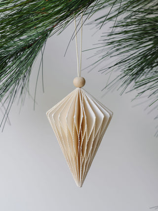 Sophisticated hand-cut paper ornament from CG Hunter, showcasing a classic diamond style, perfectly positioned against a serene backdrop of holiday pine.