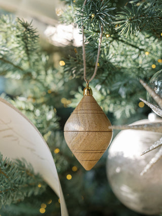 Elegant Natural Mango Wood Ornament by CG Hunter hanging on a Christmas tree, showcasing its handcrafted design and brass topper, radiating luxury and warmth.