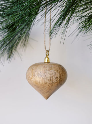 Sleek and sophisticated natural mango wood ornament by CG Hunter, suspended gracefully among pine branches.