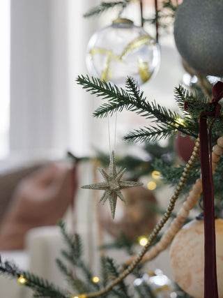 A single 2.75" Gold Glitter Starburst Ornament by CG Hunter hanging delicately amidst holiday decorations on a festive tree.