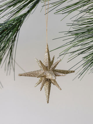 A stunning 2.75" Gold Glitter Starburst Ornament by CG Hunter, shimmering elegantly among lush green pine branches.