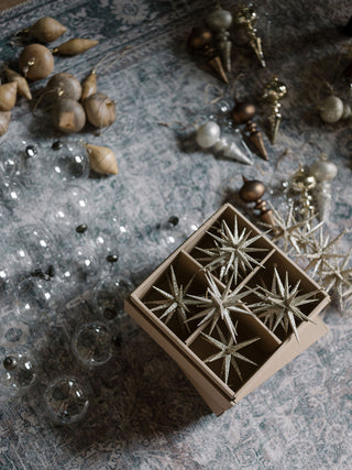 An aesthetically arranged box containing six stunning Gold Glitter Starburst Ornaments by CG Hunter, resting on a stylish patterned rug alongside elegant holiday decor, adding a touch of luxury to festive preparations.