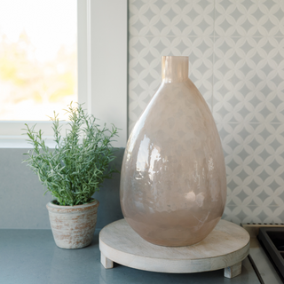 Elegant CG Hunter Handmade Hammered Glass Vase in Peach placed on a wooden stand, showcasing its artisanal craftsmanship and soft peach hue in a stylish kitchen setting.