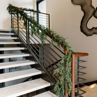 Elegant 9' Artificial Pine Garland with Pinecones by CG Hunter, beautifully draped along a modern staircase railing, enhancing the luxurious decor.