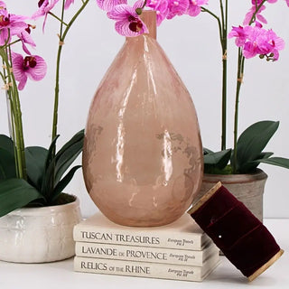 Decorative vase on books with pink flowers and a spool of thread in the background