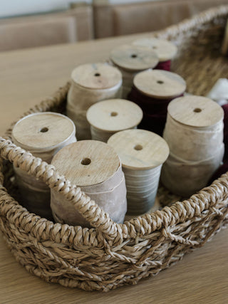 An array of spools artistically arranged in a woven basket, emphasizing the luxurious textures of CG Hunter's Hand Dyed Velvet Ribbon 10 Yards Per Spool – Set of 2.