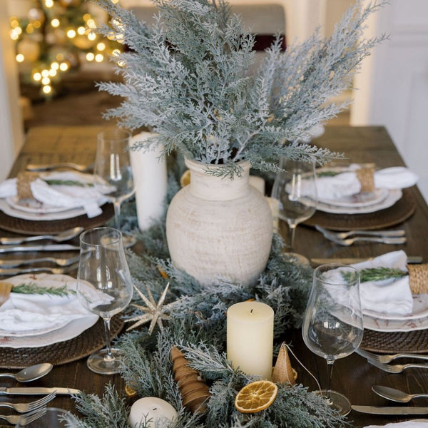 Elegant holiday table setting featuring CG Hunter 27" Flocked Cedar Stem in a stylish vase, surrounded by candles, and festive decor, creating a serene winter atmosphere.