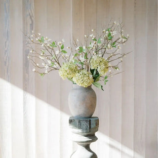 Decorative vase with greenery and white flowers against a neutral wall.