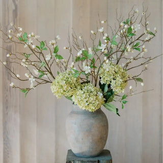 Decorative floral arrangement with green and white flowers in a textured vase against a neutral background