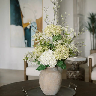 Decorative floral arrangement in a vase on a table in a room with chairs and a mirror.