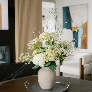 Decorative flower arrangement in a textured vase on a table with a modern interior background.