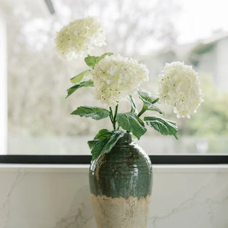 Green vase with white flowers on a marble surface