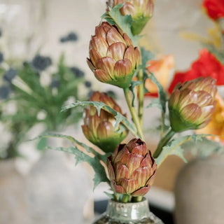Artichoke-shaped flowers in a vase with a blurred floral background