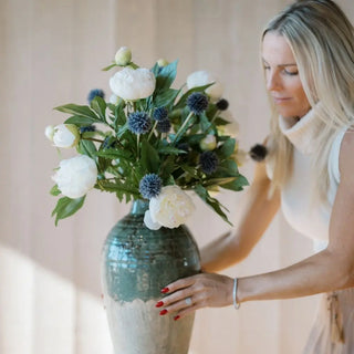 Woman holding a vase with flowers against a neutral background