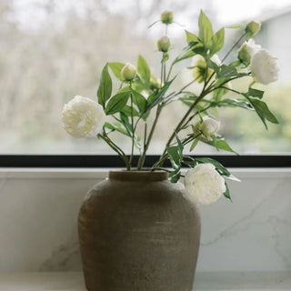 Vase with white flowers and green leaves on a windowsill