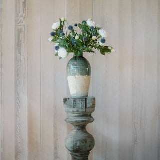 Decorative vase with flowers on a wooden pedestal against a wooden wall.