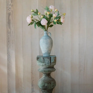 Decorative vase with flowers on a wooden pedestal against a striped wall.