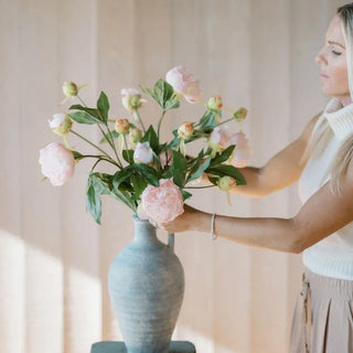 Woman holding a bouquet of pink flowers in a blue vase against a neutral background