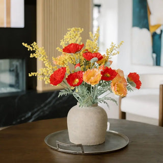 Decorative vase with red and yellow flowers on a wooden table in a living room setting.