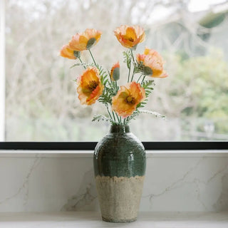 Green and beige vase with orange flowers on a windowsill