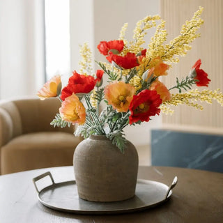 Decorative vase with red and yellow flowers on a table in a living room setting.