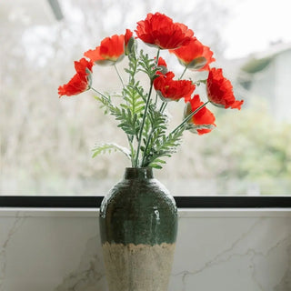 Green vase with red flowers on a marble surface