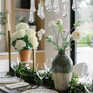 Decorative table setting with a vase of flowers and candles in a well-lit room.