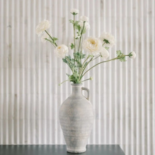 White vase with flowers on a black surface against a corrugated metal background