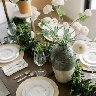 Elegant table setting with white flowers, greenery, and decorative vases.