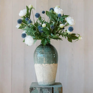 Decorative vase with green and white base holding a bouquet of flowers against a neutral background
