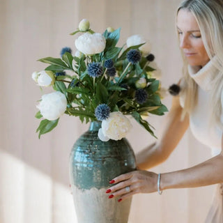 Woman holding a large green vase with white and blue flowers against a neutral background