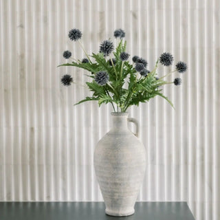 White vase with greenery and black flowers against a neutral background
