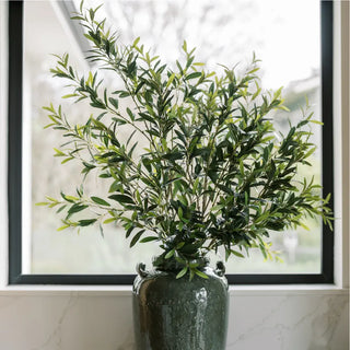 Green vase with artificial plants on a marble surface with a framed picture in the background