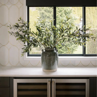 Green vase with plants on a windowsill with a decorative wall and cabinet in the background
